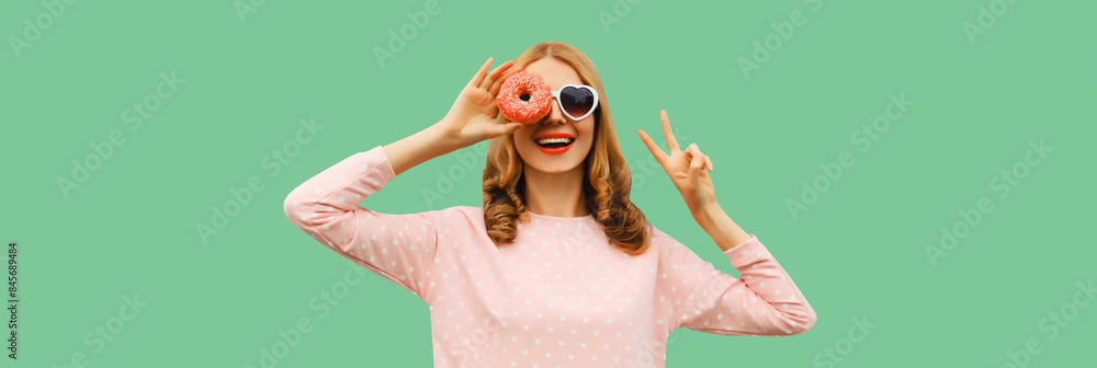 Wall mural portrait of happy cheerful laughing young woman with sweet donut having fun on green background