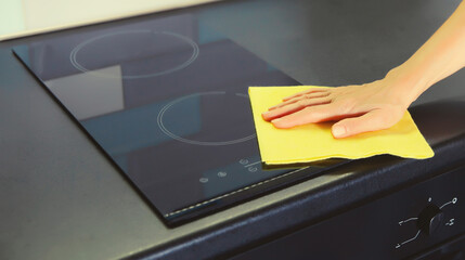 House cleaning concept - woman wiping the glass surface induction cooker kitchen countertop