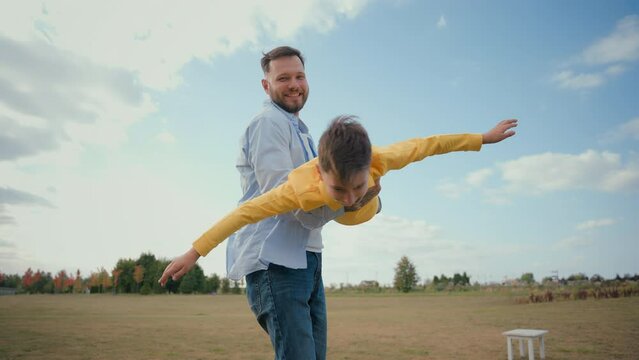 Happy Caucasian family playful laughing male man father parent dad spinning carrying arms holding spin whirling little boy son child kid swing play plane flying game having fun rural nature field farm