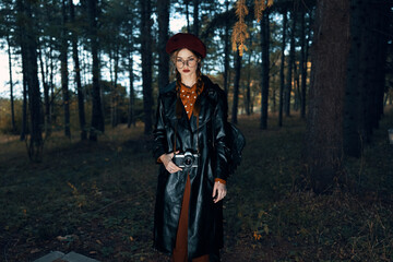 Mysterious woman in black coat and red hat stands alone in enchanted forest clearing