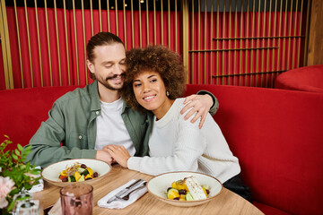 An African American woman and a man sit at a table, enjoying plates of food in a modern cafe.