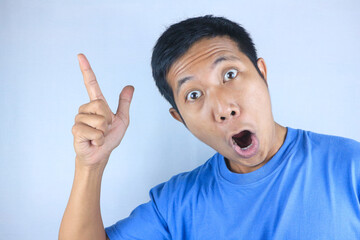 funny facial expression of shocked young asian man pointing up direction, promoting product