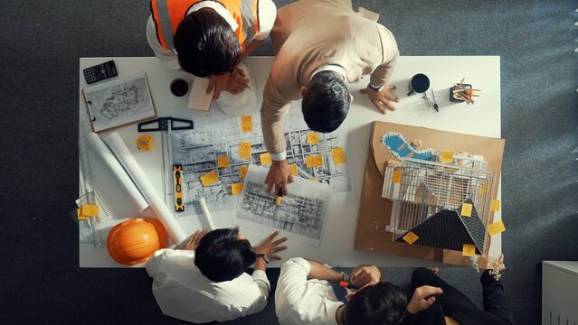 Top down view of skilled engineer team compare between blueprint and house plan. Aerial view of group of architect or designer discussing and point note to brainstorm about blueprint. Alimentation.