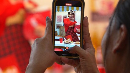 Customer record video of restaurant worker dancing and holding food tray at modern bar with food. Male asian waitress with napkin preparing food order while customer hands holding camera. Regalement.