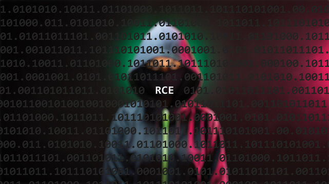Cyber attack rce text in foreground screen, anonymous hacker hidden with hoodie in the blurred background. Vulnerability text in binary system code on editor program.