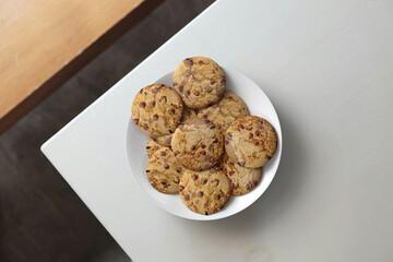 Delicious chocolate chip cookies on a wooden table, top view. Some cookies on the white bowl.