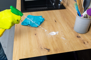 Person, hands and cleaning table with spray bottle in kitchen hygiene, germ or bacteria removal at home. Closeup of maid or cleaner wiping counter with cloth and detergent in healthy disinfection