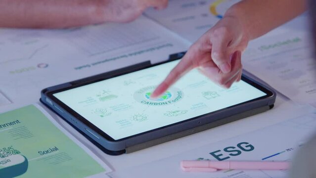 close up diversity team brainstorming focused on ESG (environment,social,governance) carbon footprint with tablet or sdgs goals in a sustainable green office at night