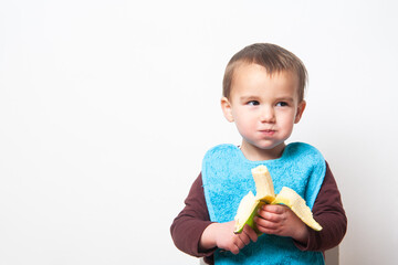 Toddler with blue bib eating banana. Children and food.