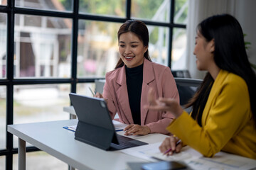 Two women are sitting at a table with a laptop and a tablet