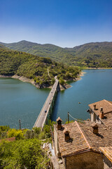 Obraz premium A view of Lake Turano, from the village of Castel di Tora, Rieti, Lazio, Italy. The bridge crossing the lake, surrounded by green mountains. Blue sky in summer.