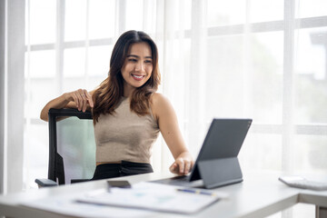 A woman is sitting at a desk with a laptop and a tablet