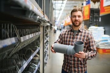 male plumber in a hardware store chooses the sewer pipes, the concept of plumbing work in the house