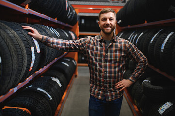 Male mechanic holding car tire in automobile store
