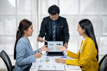 Three women and a man are sitting around a table with papers and laptops