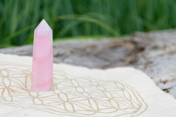 An image of a tall rose quartz crystal tower on a crystal grid cloth using the flower of life sacred geometry. 