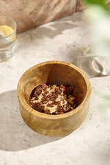 Traditional Russian Sour Cream and Caramel Dessert with Chocolate Sponge in Wooden Bowl, Sunlight on Beige Table
