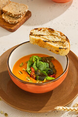 Delicious Pumpkin Cream Soup with Fresh Greens and Toasted Bread on Rustic Table