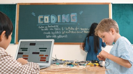 Asian boy coding program while caucasian friend fixing electric board at STEM class. Energetic...