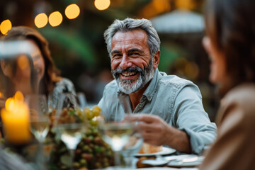 Mature Man Laughing While Enjoying an Evening Dinner with Friends