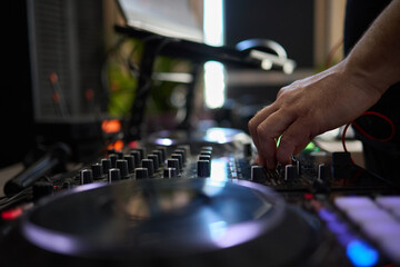 control DJ for mixing music with blurred people dancing at party in nightclub.