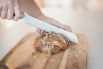 A man cuts a whole grain bread with a knife in the kitchen