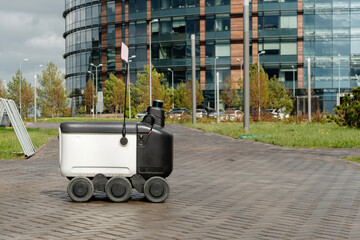 Modern automated delivery robot stands outside waiting for an order in rainy weather. Modern...