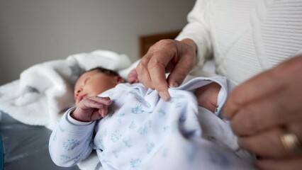 Newborn baby being carefully dressed in a soft white onesie by gentle hands. baby lies peacefully on a soft blanket, showcasing tender caregiving moments and early stages of life