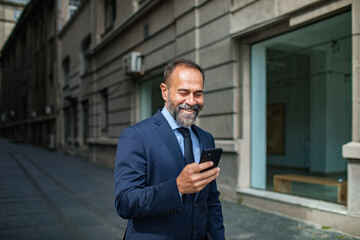 Smiling businessman in a suit holding a smartphone in city