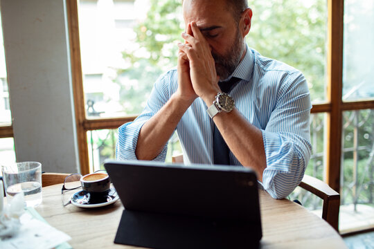 Stressed businessman working on a tablet in a cafe