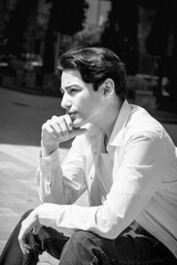 Young man model sits on steps in city. Casual, fashion. BW grainy photo