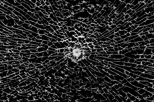 Texture of broken tempered glass with a bullet hole and diverging cracks on a black background. Design element.