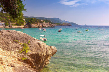 Small boats in clear waters of Paleokastritsa Bay in Corfu, Greece, surrounded by rocky cliffs
