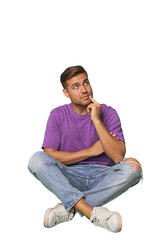 Obraz premium Casual man sitting on floor looking sideways with doubtful and skeptical expression.