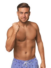 Fototapeta premium Young man shirtless in swimwear, studio showing fist to camera, aggressive facial expression.