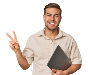 Fototapeta na wymiar Man holding laptop, studio joyful and carefree showing a peace symbol with fingers.