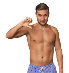 Fototapeta premium Young man shirtless in swimwear, studio showing a dislike gesture, thumbs down. Disagreement concept.