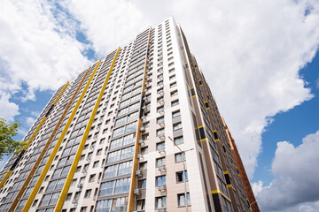 A modern highrise residential building embodies contemporary urban living in a bustling city, set against a blue sky with fluffy clouds, showcasing the dynamic skyline