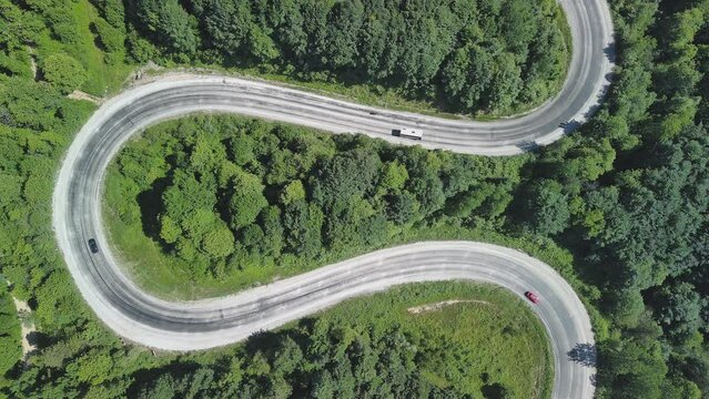 Aerial view of winding asphalt mountain road among green trees in summer.