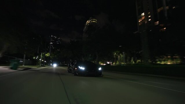 Rolling shot of  black supercar driving at night on the streets in Miami Florida city with skyline city lights view