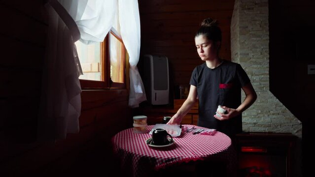 Girl Setting Breakfast Table in Rustic Wooden House. Young Woman Preparing a Cozy Breakfast in a Countryside Cabin