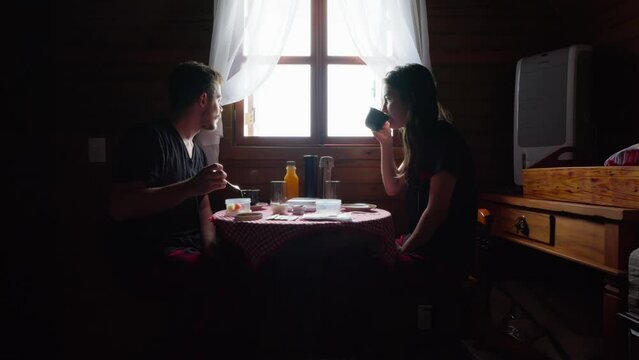 Couple Having Breakfast in Rural Wooden House. Morning Routine. Lovers in Pajamas Enjoying Breakfast and Sunrise in a Cozy Cabin