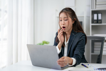 Businesswoman in a suit surprised while working on laptop in office, expressing shock or amazement,...