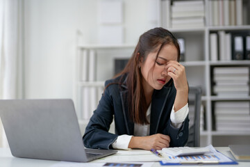 Stressed businesswoman in office with laptop, holding head in frustration. Overworked professional facing challenges and deadlines.