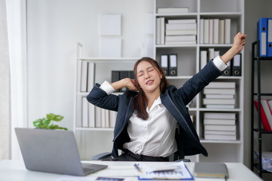 Young businesswoman stretching and relaxing at her desk in a modern office, showcasing a work-life balance in a professional setting.