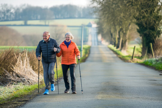 Elderly couple Nordic walking on country road, showing active lifestyle in beautiful setting.  Senior Citizens Day