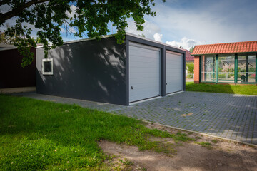 a newly built double garage with roller doors stands under a tree