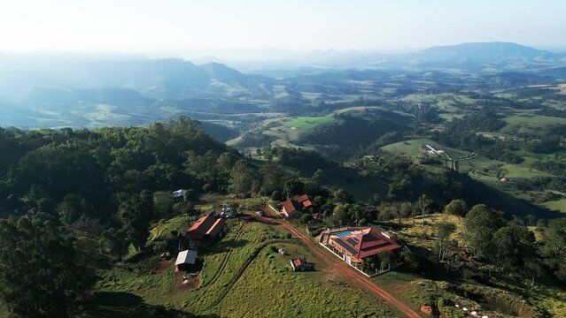 Aerial Shot of a Countryside Property with Solar Panels, Green Vegetation, and Mountain Backdrop. Drone View of a Farmhouse in a Sunny Rural Landscape