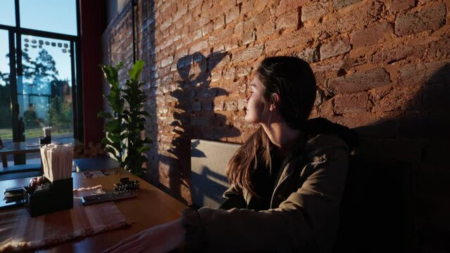 Serene Moment of a Young Woman Sitting at a Caf&eacute; Table, Admiring the Sunset. Girl in Caf&eacute; Gazing at Sunset Horizon 