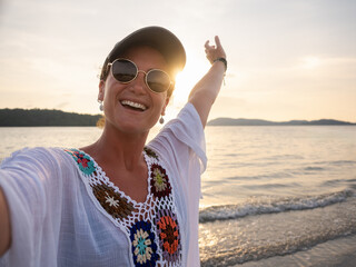 Cheerful Woman in Crochet Top Taking Selfie at Sunset on Tropical Beach Stretching her Arm with Joy